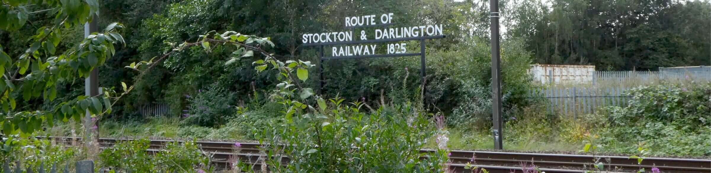 A sign behind a railway track saying Route of Stockton & darlington Railway 1825