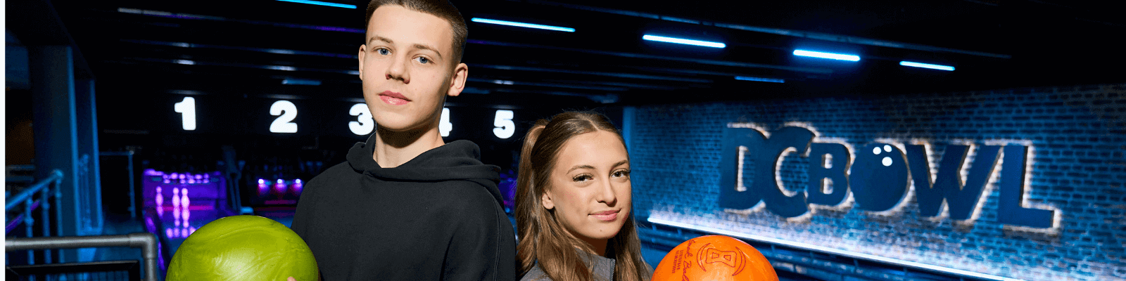 A teenage boy and girl holding bowling balls at DC Bowl