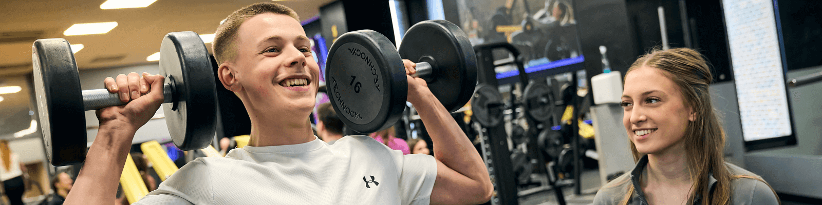 Two teenagers at the gym with one holding dumbells