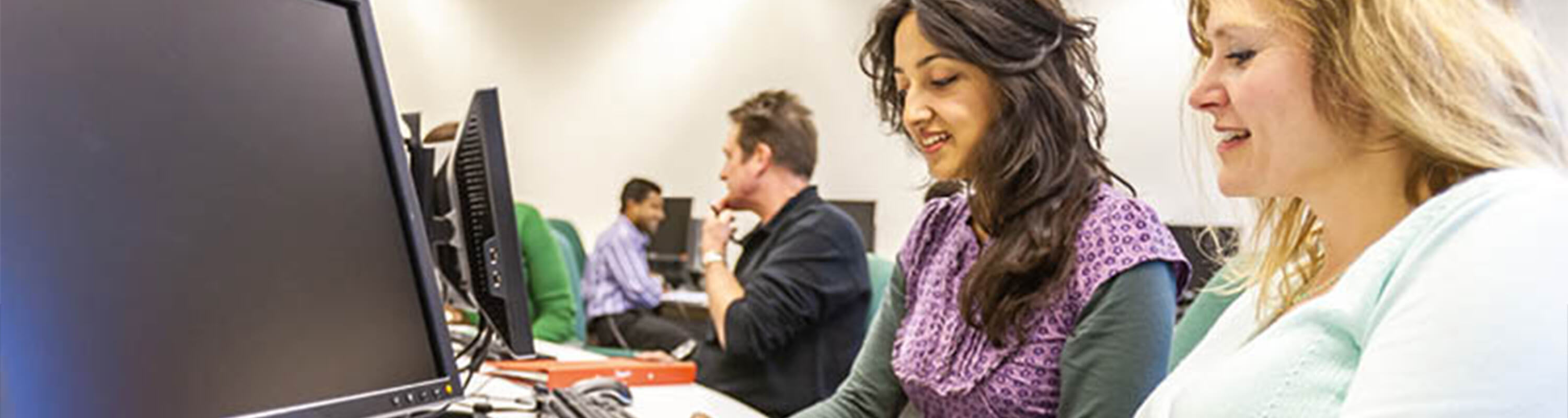 A group of learners sit next to desktop computers