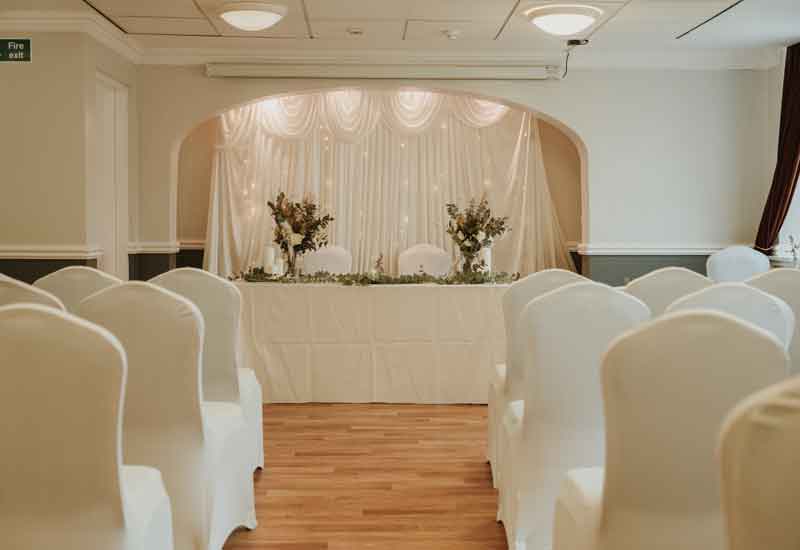 Room set out for wedding ceremony with whote cloth covered chairs