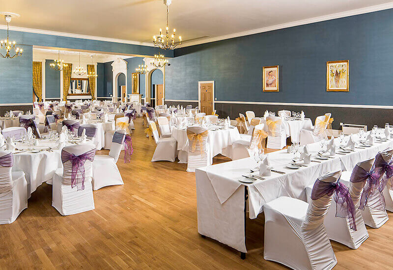 Large room set out with tables and chairs covered n white cloth for wedding reception