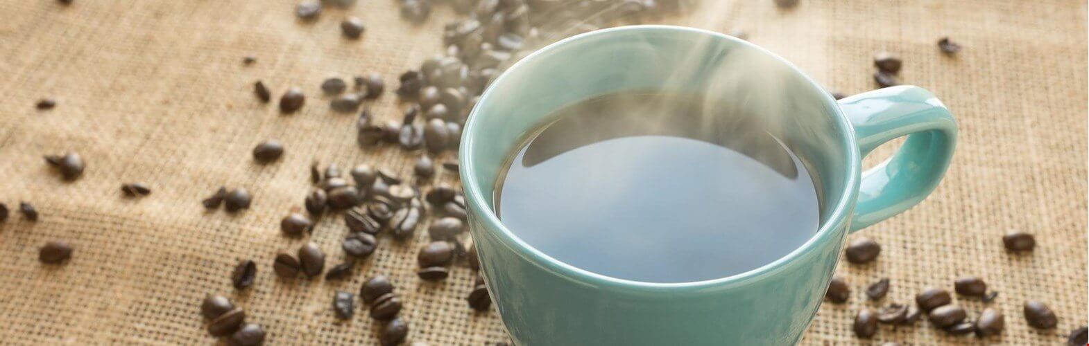A black coffee in a white mug with coffee beans scattered around it